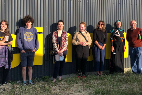 A group of 7 smiling people stand outside of a cinema for a group photo.